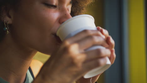 close up of female customer in coffee shop window drinking hot drink