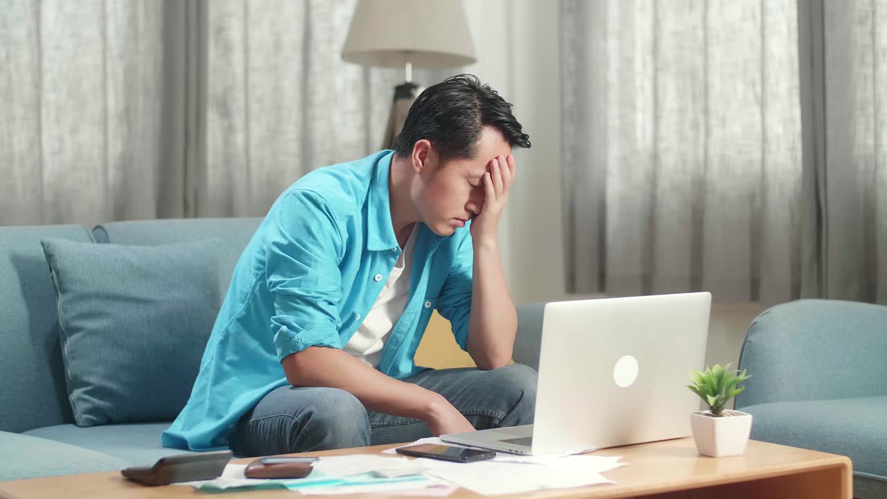 소파에 앉아 슬프고 있는 노트북을 가진 아시아인