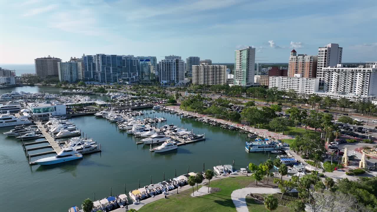 Marina Port of Sarasota with parking yachts and traffic on coastal road in Sarasota, Florida. Aerial wide shot. Skyline and Skyscraper towers against blue sky. Residential area of noble district in FL