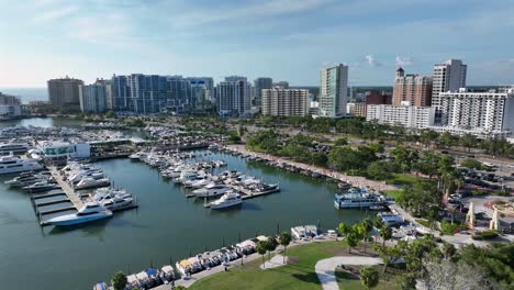 marina port of sarasota with parking yachts and traffic on coastal road in sarasota, florida. aerial wide shot. skyline and skyscraper towers against blue sky. residential area of noble district in fl