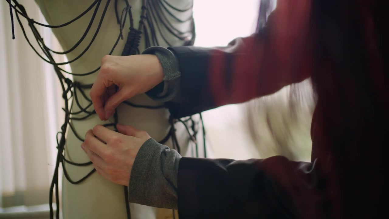Nahaufnahme einer Person, die Kordeln oder Stoff an einer Schneiderpuppe anpasst.