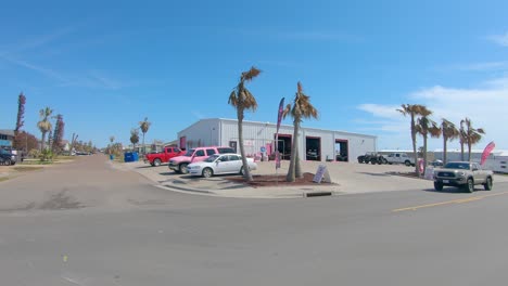 POV-driving-past-a-car-repair,-hotel-and-tourist-shops-on-a-bright,-sunny-day-during-spring-break-in-Port-Aransas,-Texas