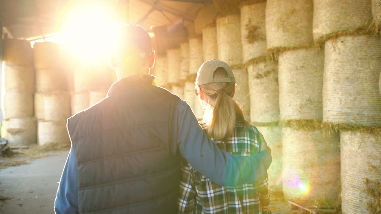 вид сзади на кавказскую молодую пару, идущую по конюшне с запасами сена