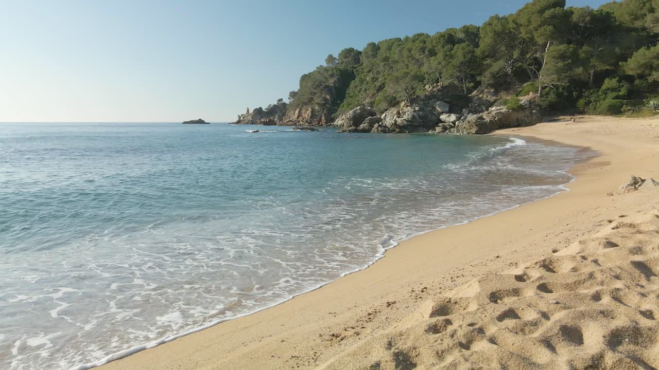 Onde di acqua cristallina che si infrangono su una spiaggia esotica e sabbiosa a Lloret de Mar, Spagna