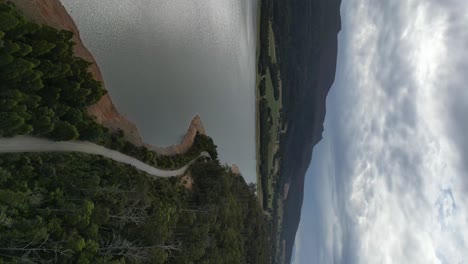 Vertical-flight-over-street-along-Huntsman-Lake-during-cloudy-day-in-Tasmania,-Australia