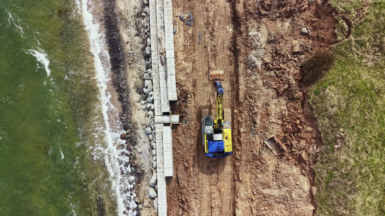 Lavori di costruzione sul litorale in una zona costiera con macchinari pesanti e acqua limpida visibile in una giornata di sole.
