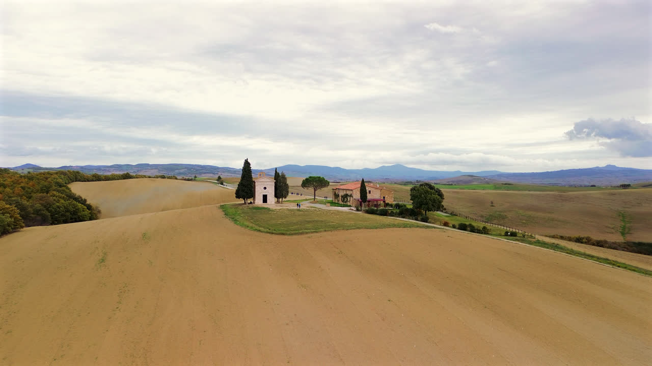 Aerial of dirt road through Tuscan farmland with soft clouds and warm light in renaissance