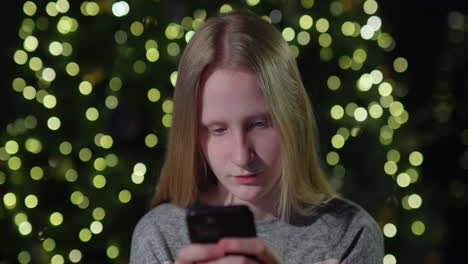 a teenage girl uses a smartphone on the background of a christmas tree