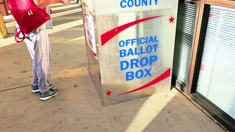 woman votes for president by dropping mail-in ballot letter in slot at official ballot drop box sign for voting in american democratic election