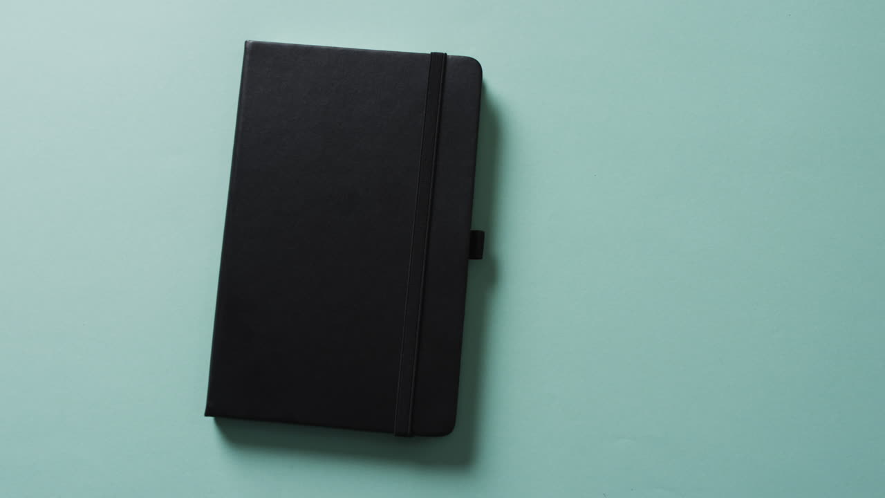 Close up of closed black notebook with copy space on green background in slow motion