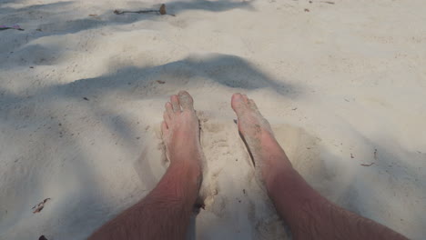 pov shot of the male legs digging in the clear white sand on the beach