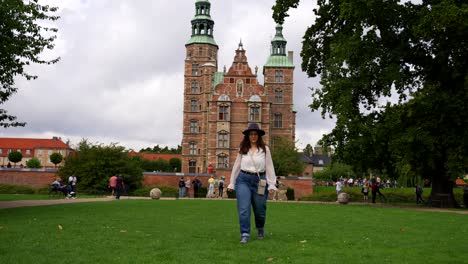 woman with casual clothes and hat walks towards camera near rosenborg castle