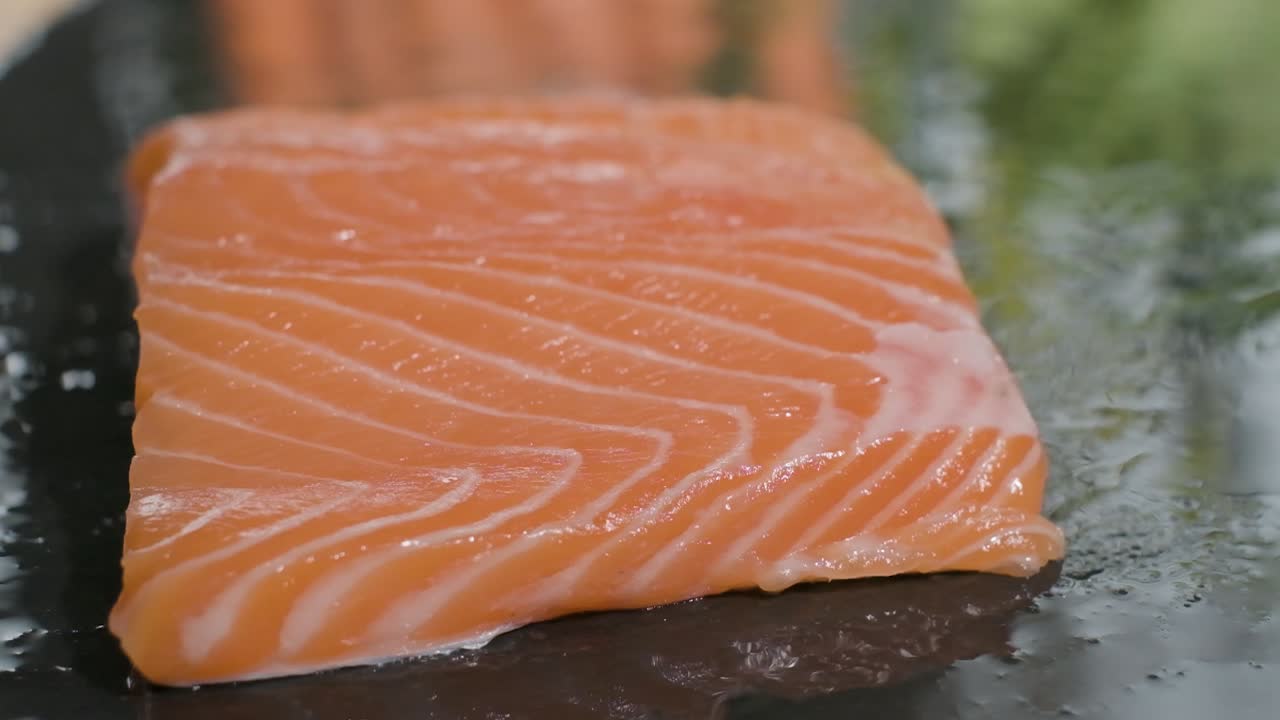 filete de salmón fresco que cae en una tabla de piedra negra mojada