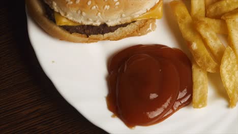 hand dipping french fries into ketchup with a burger and fries