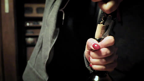 mujer con esmalte de uñas rojo sacando el corcho de una botella de vino.