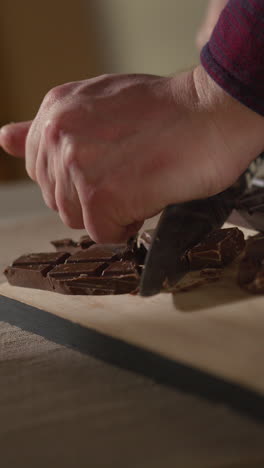 vertical video of person cutting bars of milk plain and white chocolate into smaller pieces with knife