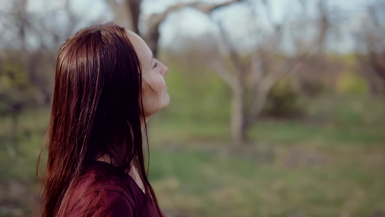 una joven morena de cabello largo se para entre los árboles y medita. los ojos cerrados, disfrutando de la naturaleza. movimiento circular de la cámara.