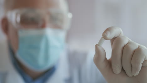 extreme close-up of a masked scientist developing a coronavirus vaccine holding a white pill. the doctor looks at the painkillers antiviral medication. vitamins. high quality 4k footage