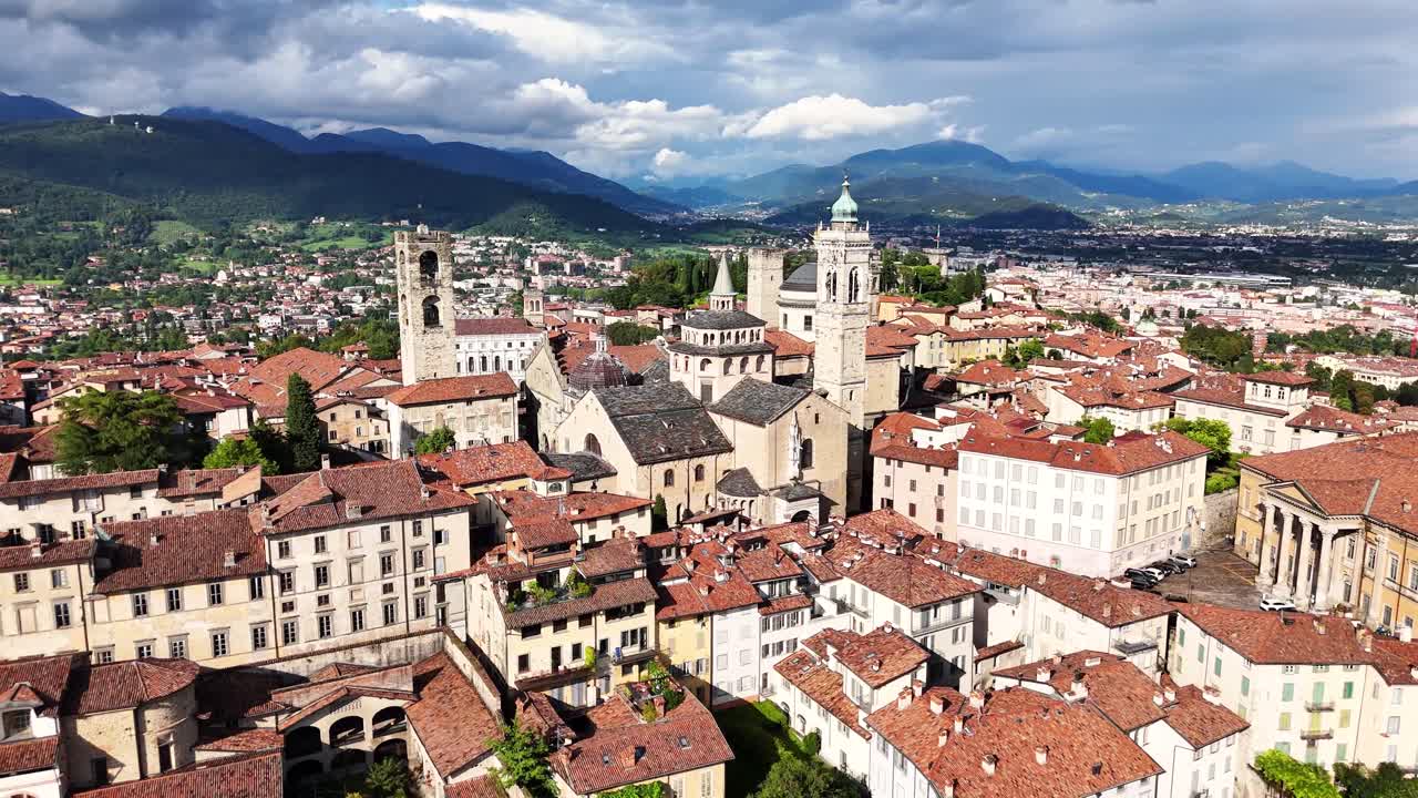 Drone orbiting Bergamo Citta Alta, showcasing dome of the Bergamo Cathedral and the distinctive bell tower of the Basilica of Santa Maria Maggiore, nestled among historic red-tiled rooftops