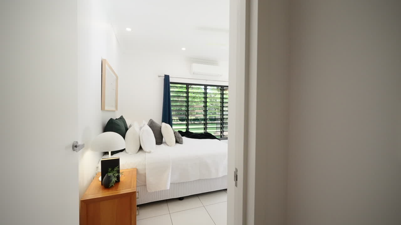 열대 뒷마당으로 갈 수 있는 슬라이딩 문이 있는 멋진 마스터 침실을 드러내기 위해 문 프레임을 밀어 넣습니다.