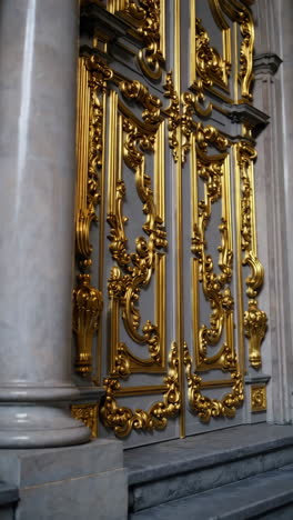 ornate gold doors with marble columns and staircase
