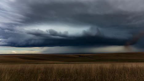 dramatic stormy sky with a tornado or dust devil over rolling hills and a field