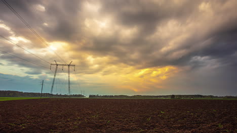 silhouette of high voltage power line pole against sunset stormy sky, time lapse