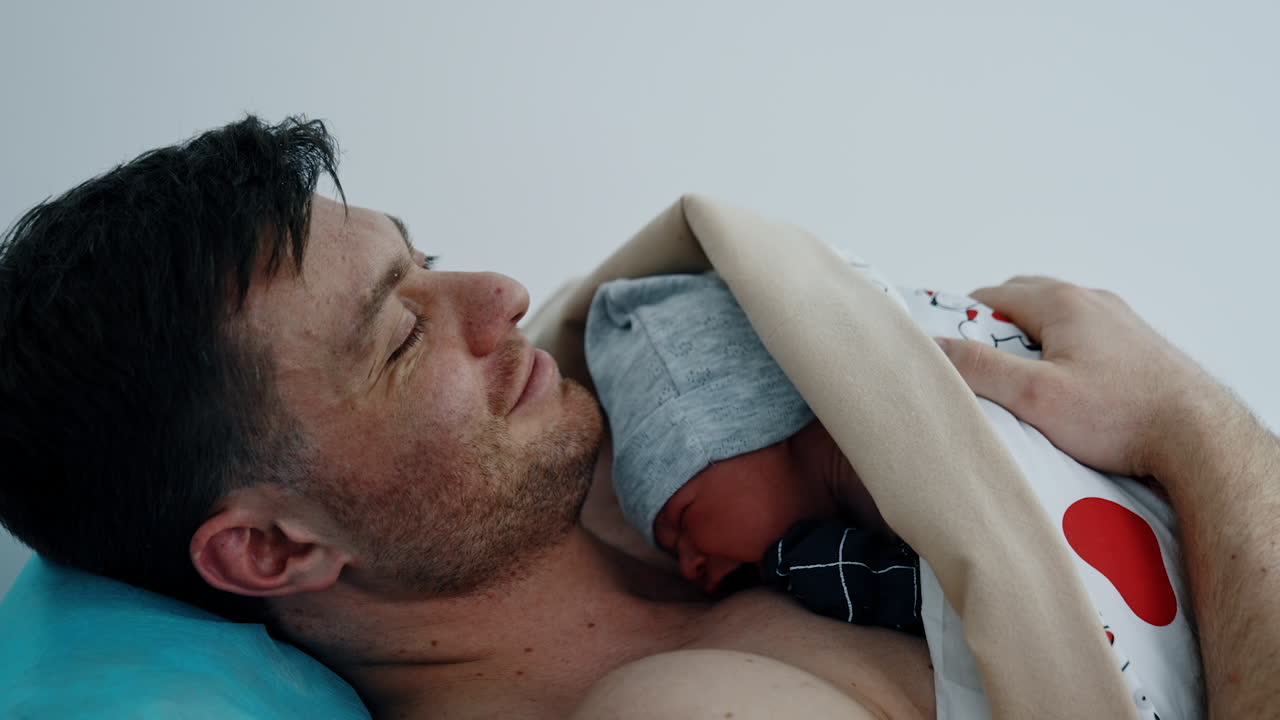 Skin to skin contact of a newborn with a father. Man is smiling happily to hold his baby for the first time. Close up.