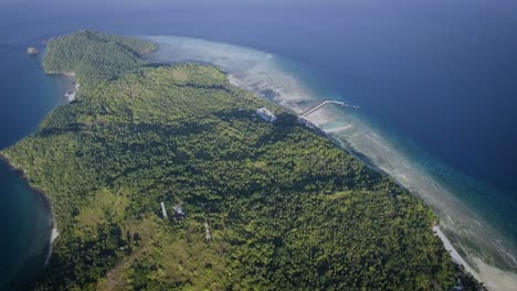 aerial shot of small island with a small village and a jetty, surrounded by blue ocean in the afternoon