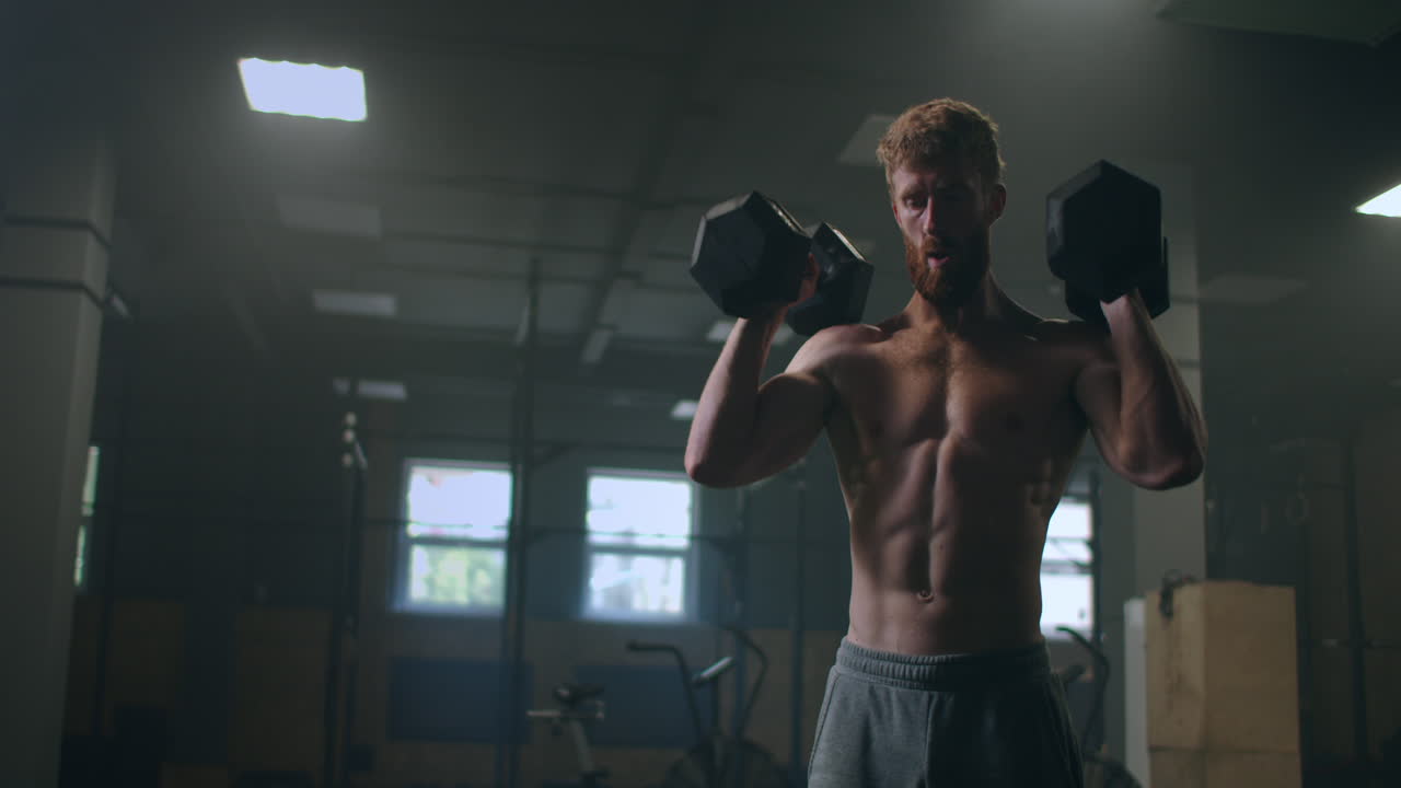 Un uomo senza maglietta si allena sollevando manubri in palestra. Un atleta robusto e atletico.
