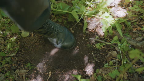 leg view of tourist swinging left boot with sand while standing on dry leaf and grass covered forest ground under canopy with dappled shadows conveying moment of relief during outdoor adventure
