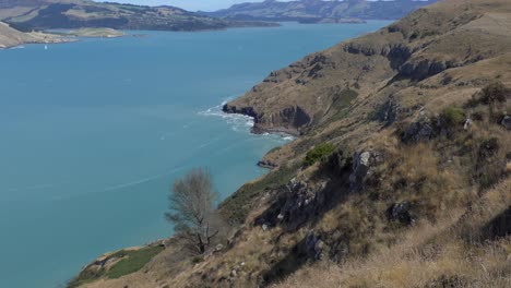 Aufwärts-Rollen-über-Karge-Landschaft,-Kontrastiert-Mit-Wunderschönem-Türkisfarbenem-Wasser-Und-Blauem-Himmel-–-Lyttelton-Harbour,-Neuseeland