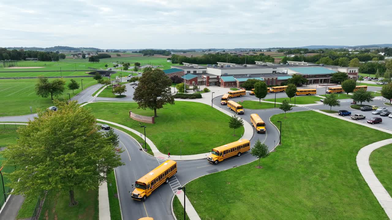 Line of yellow school buses exiting an American school campus on a cloudy day