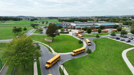 line of yellow school buses exiting an american school campus on a cloudy day