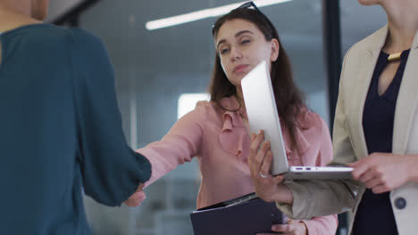 mujer de negocios caucásica de pie y estrechando la mano con una colega en una reunión en la oficina