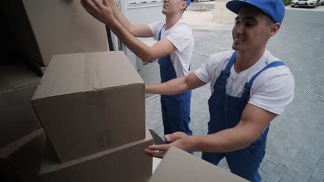 Two young workers of removal company are loading boxes and furniture into a minibus