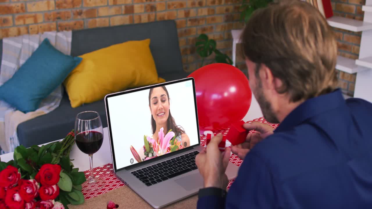 Casal caucasiano em videochamada de Dia dos Namorados, homem mostrando anel para mulher sorrindo na tela do laptop.