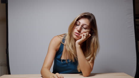 close-up of a woman leaning on a table in studio, first placing her hands on her shoulders, then shifting her pose, resting on one hand, then the other