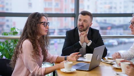 beautiful curly-haired lady in glasses sits in front of laptop and speaks to her partners. colleagues talk about professional issues at coffee time.