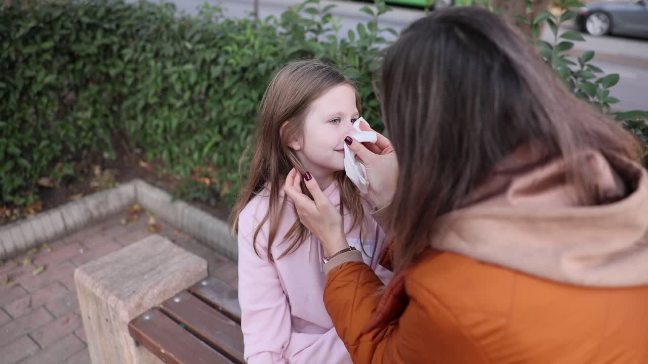 Mother cleaning daughter's face with a tissue on a bench