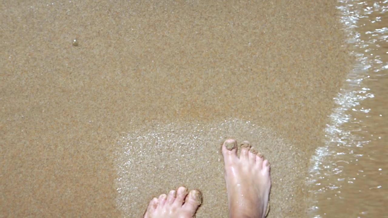 POV of Bare Feet Walking on Sandy Beach with Gentle Waves