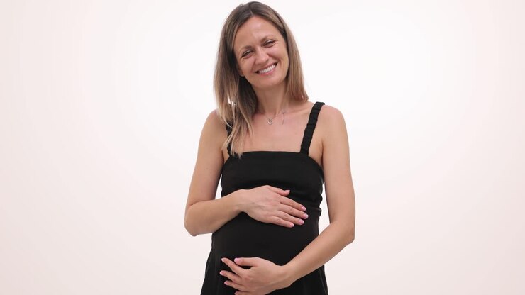 A smiling pregnant woman in a black dress holding her baby bump