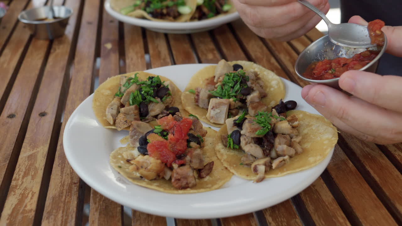 Hænder der skovler salsa på traditionelle mexicanske street tacos, nærbillede
