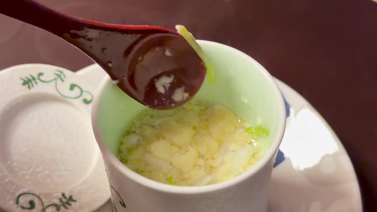 Foto close-up seseorang yang sedang menyendok kustar telur Jepang kukus dari cangkir keramik.