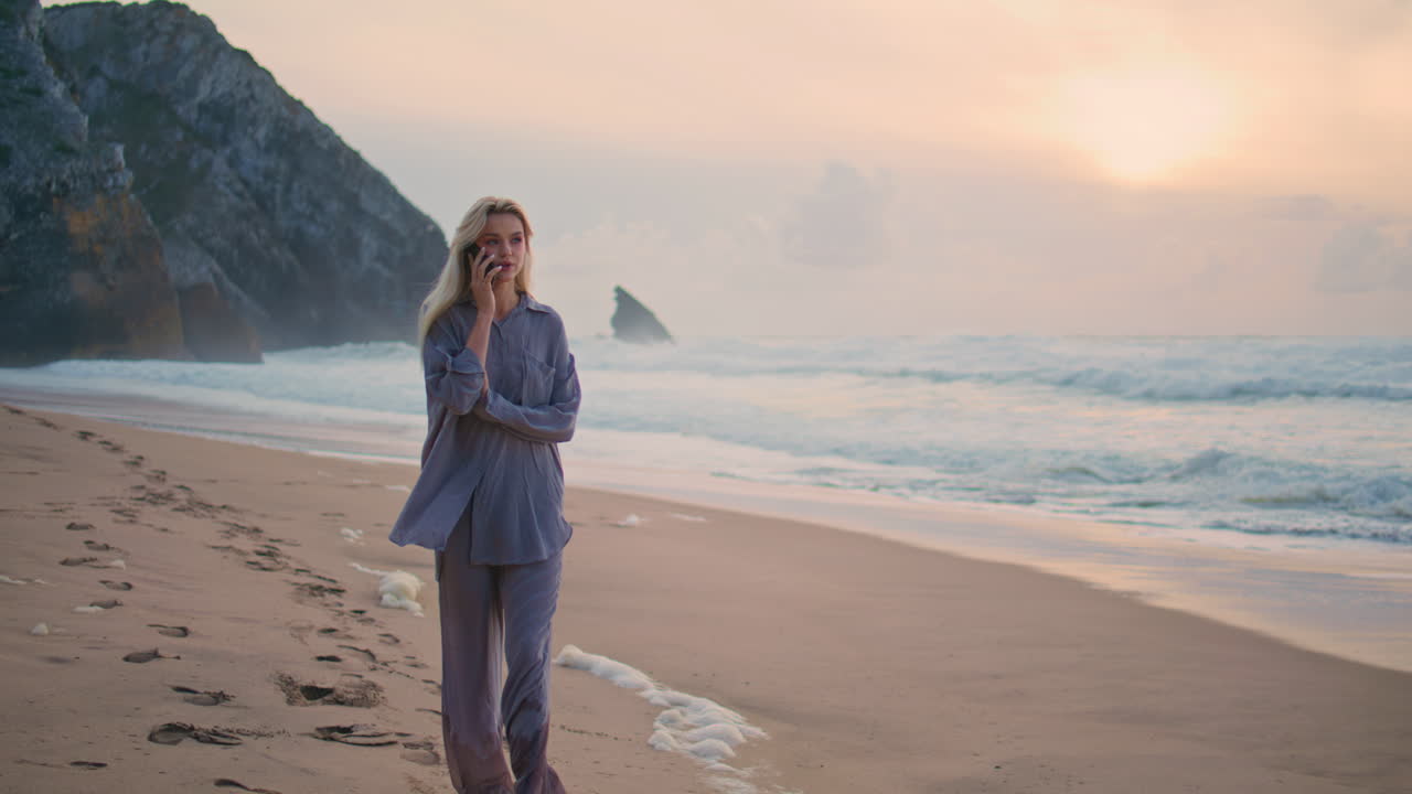 Bella viaggiatrice che parla al cellulare sulla riva al tramonto nuvoloso. Ragazza calma che ammira.