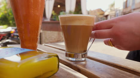 una mano alcanzando lentamente un vaso de café latte en un café al aire libre, capturado en cámara lenta, retratando un momento relajante