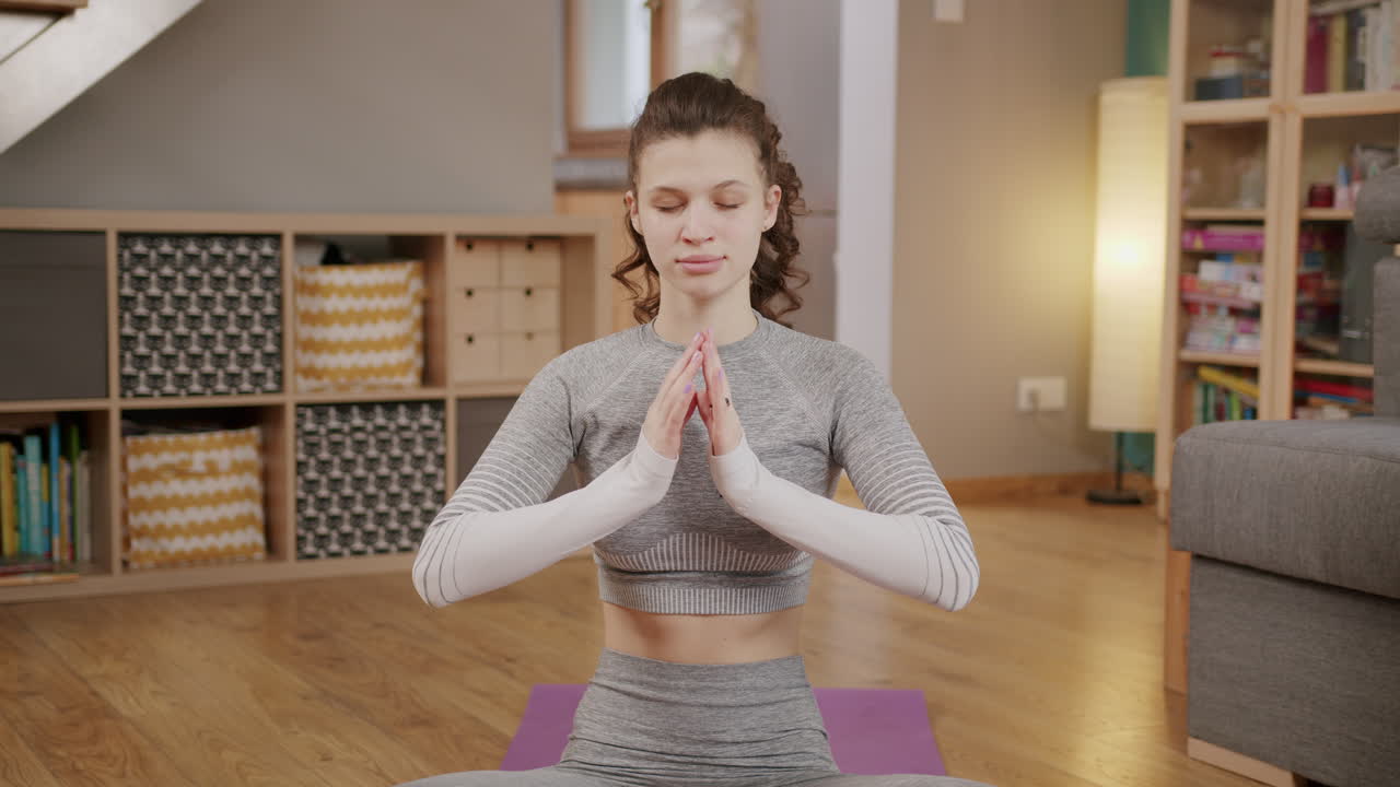 vista frontal estática de una mujer joven con los ojos cerrados haciendo yoga en casa