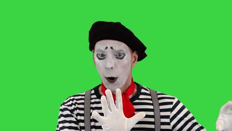 young funny mime behind an invisible wall on a green screen, chroma key