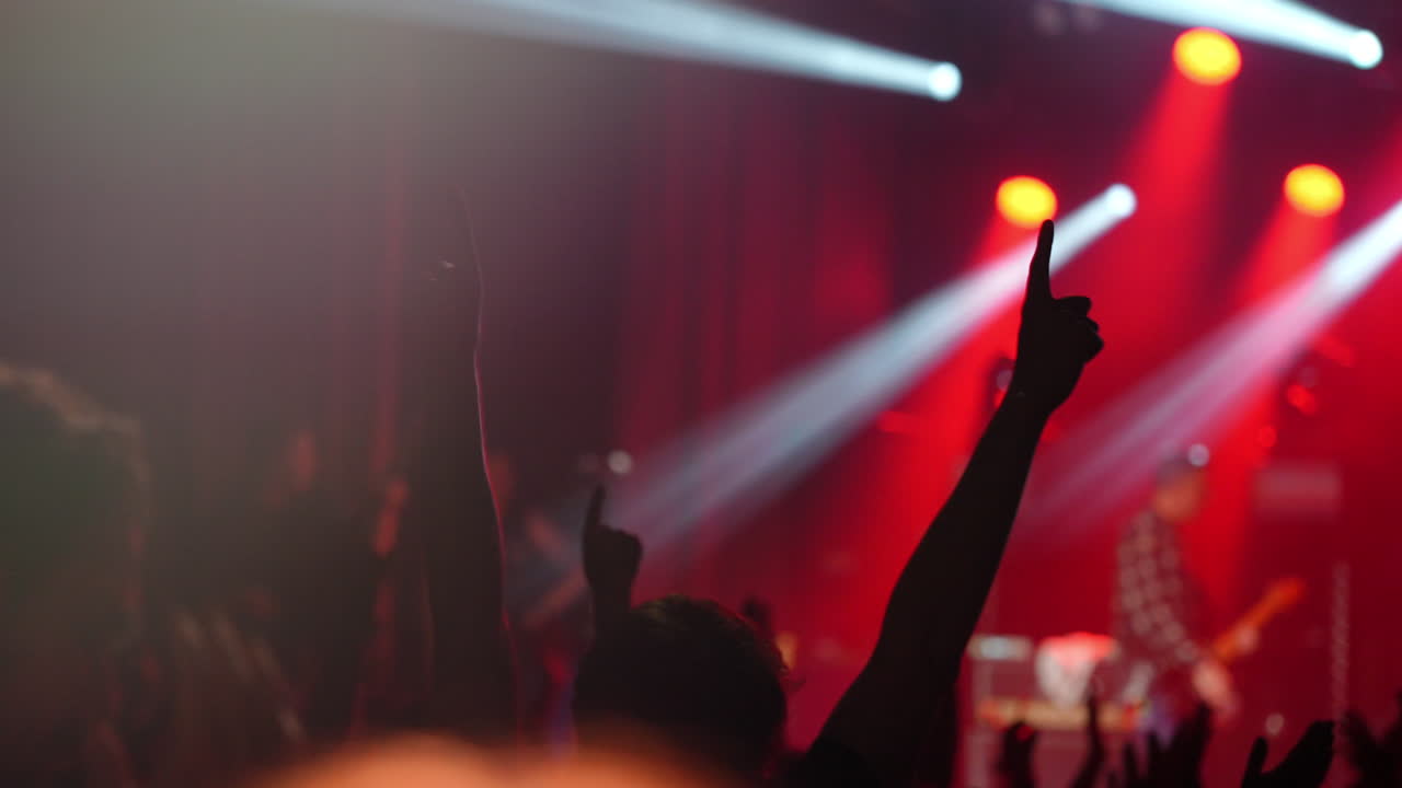 Enthusiastic crowd at a live concert with raised hands and vibrant stage lighting effects