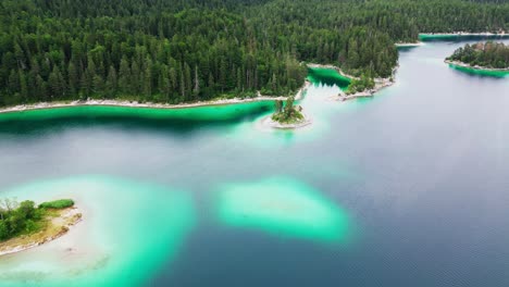 an aerial view of a luminescent turquoise lake, with islands, surrounded by emerald pine trees